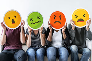 quatre personnes assise portant chacune un emoji représentatif d'une émotion négative, peur, colère, angoisse et surprise