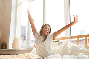 une jeune femme dans son lit semble se réveiller en pleine forme et s'étire comme une bien heureuse et reposée
